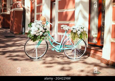 Vélo modèle femelle bleu vif avec fleurs garées près du bâtiment par une journée ensoleillée Banque D'Images