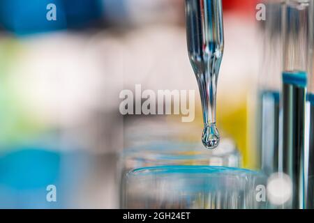 Goutte de liquide bleu de la goutte d'eau au tube à essai en laboratoire avec un arrière-plan de couleur vive et flou. Concept d'extrait pur et propre. Banque D'Images