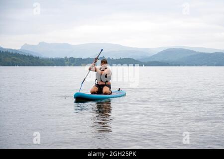 Jeune homme paddle-Boarding sur Windermere dans le parc national de Lake District, Royaume-Uni Banque D'Images