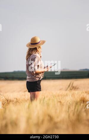 Agricultrice debout dans le champ de l'orge et examinant la qualité des produits avant la récolte. Femme utilisant une tablette numérique pour une agriculture intelligente Banque D'Images