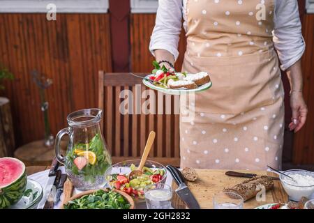 Dégustez une salade de légumes frais et une baguette au fromage cottage. Femme servant de la nourriture végétarienne sur l'assiette lors d'une fête ou d'un événement de célébration dans le jardin Banque D'Images