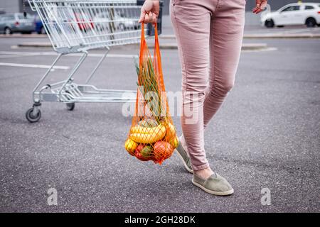 Femme avec sac en filet réutilisable marchant du chariot dans le parking à côté du supermarché. Concept sans plastique et sans déchets. Achat d'articles d'épicerie Banque D'Images