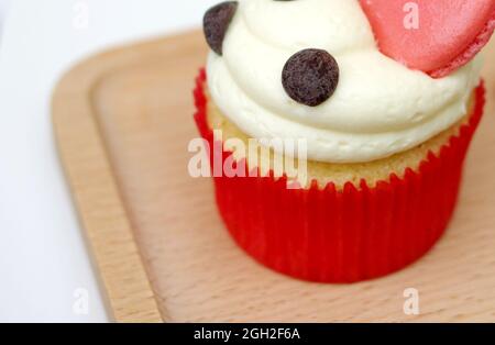 Cupcake à la crème vanille avec Macron rose et doublure en papier rouge sur une assiette en bois Banque D'Images