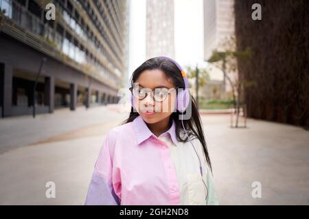 Portrait de jeunes Afro-américains portant des lunettes écoutant de la musique avec des écouteurs sur fond urbain dans la ville. Habillé de couleurs Banque D'Images