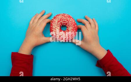 Le concept idéal pour la création alimentaire. Photo d'un délicieux donut aux touches colorées et aux deux mains de bébé. Isolé sur fond bleu pastel Banque D'Images