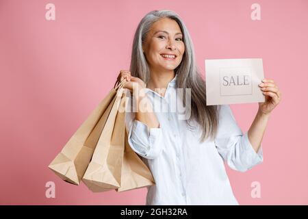 Belle femme d'âge moyen tient des sacs de papier et de carte avec le mot sale en studio Banque D'Images