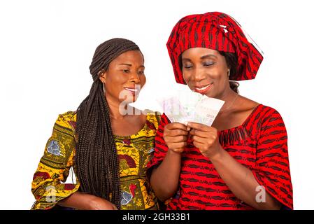 deux belles femmes d'affaires debout dans une robe traditionnelle sur fond blanc regardant les billets de banque souriant. Banque D'Images
