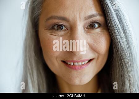Joyeuse femme aux cheveux argentés avec maquillage regarde dans l'appareil photo sur fond gris clair Banque D'Images