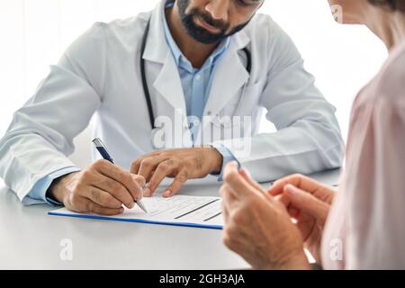 Médecin indien de sexe masculin consultant un ancien patient senior remplissant un formulaire médical. Banque D'Images