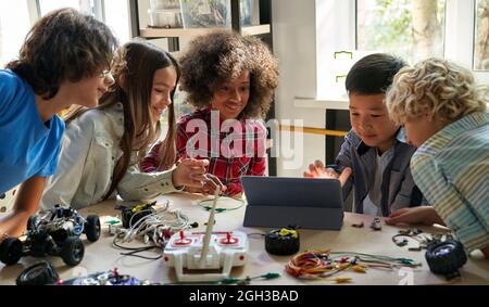 Heureux divers élèves de l'école construisant des voitures robotisées à l'aide d'un ordinateur. Banque D'Images