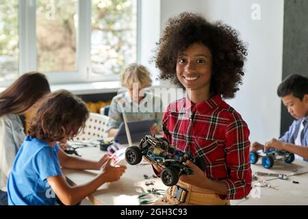 Bonne fille afro-américaine d'école de gamin tenant une voiture robotique à la classe STEM. Banque D'Images