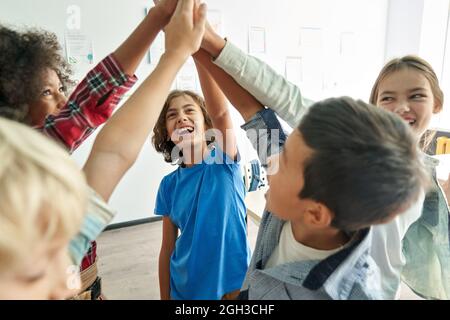 Joyeux groupe d'élèves divers d'école d'enfants donnant les cinq hauts ensemble dans la salle de classe. Banque D'Images