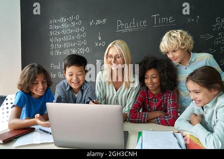 Heureux divers élèves de l'école se réunissent à table d'enseignant regarder l'ordinateur portable. Banque D'Images