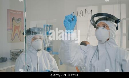 Des spécialistes dentaires analysent l'écran des comprimés et écrivent sur du verre pour obtenir des informations sur l'examen de la dentisterie. Dentiste utilisant un marqueur noir pour les notes de dentisterie expliquant l'opération à l'infirmière Banque D'Images