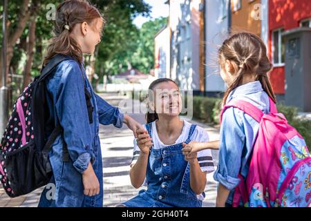 Une jeune femme soutient moralement les filles qui tiennent la main encourage les enfants, accompagne les élèves à l'école. Banque D'Images