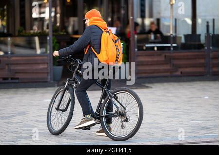 Riga, Lettonie - 3 septembre 2021 : un jeune homme dans un chapeau de couleur vive et avec un sac à dos sur un vélo dans une zone pavée près d'un café Banque D'Images