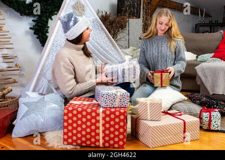 jeunes filles ayant plaisir emballer des cadeaux à la maison, grand travail d'équipe d'amis emballer des cadeaux pour noël, se préparer pour le prochain an et noël Banque D'Images