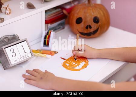 Préparation pour halloween. calendrier en bois avec la date 31 sur la table d'école. Citrouille avec un visage effrayant. Fille tire une carte de citrouille pour Halloween. Banque D'Images