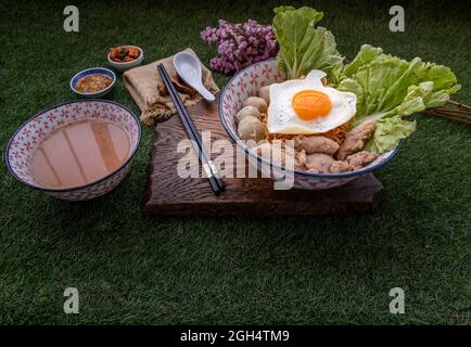 Faire bouillir les nouilles aux œufs avec de la boule de porc, du porc haché, des œufs frits, des légumes et des soupes dans un bol et un bâtonnet à base de cuillère et de bois. Soupe de nouilles thaï Banque D'Images
