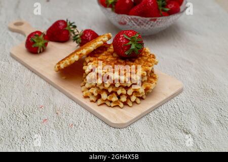 Gaufres servies avec des fraises sur une planche à découper blanche sur une table grise et un panier de fraises mûres Banque D'Images