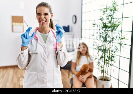 Jeune médecin femme mettant le vaccin à la petite fille collant la langue dehors heureux avec l'expression drôle. Banque D'Images