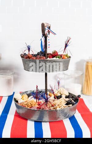 Le 4 juillet, un plateau de charcuterie est servi sur un support métallique à deux niveaux rempli de fromage, de craquelins, de salami et de fruits frais Banque D'Images