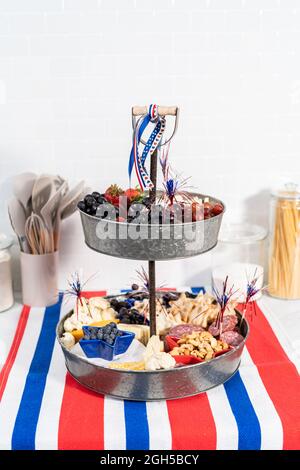 Le 4 juillet, un plateau de charcuterie est servi sur un support métallique à deux niveaux rempli de fromage, de craquelins, de salami et de fruits frais Banque D'Images