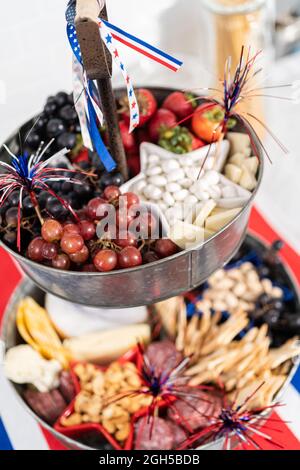 Le 4 juillet, un plateau de charcuterie est servi sur un support métallique à deux niveaux rempli de fromage, de craquelins, de salami et de fruits frais Banque D'Images