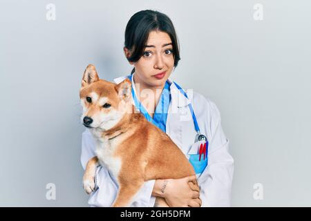 Belle femme vétérinaire hispanique tenant chien sceptique et nerveux, frowning bouleversé à cause du problème. Personne négative. Banque D'Images