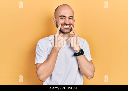 Jeune homme bald portant un t-shirt blanc décontracté souriant avec la bouche ouverte, les doigts pointant et forçant sourire joyeux Banque D'Images