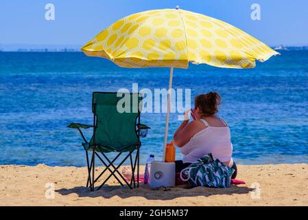 Une femme en surpoids assise sur la plage sous un parasol Banque D'Images