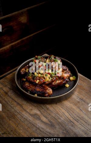 Au-dessus de délicieuses ailes de poulet rôties dans une sauce barbecue décorée avec des légumes frais servis sur une assiette sur une table en bois au restaurant Banque D'Images