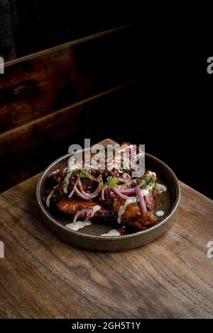 Au-dessus de délicieuses ailes de poulet rôties dans une sauce barbecue décorée avec des légumes frais servis sur une assiette sur une table en bois au restaurant Banque D'Images