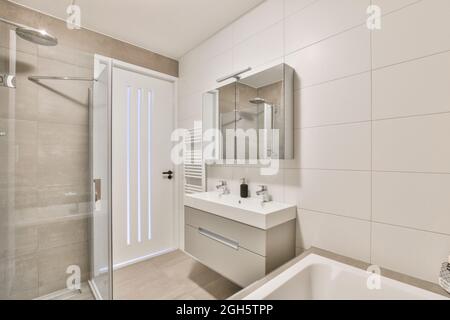 Intérieur de la salle de bains avec miroir suspendu sur double lavabo placé près de la porte d'entrée et cabine de douche en verre dans l'appartement moderne Banque D'Images