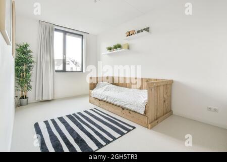 Décoration moderne de style minimaliste, chambre blanche au design écologique avec lit simple en bois et moquette rayée avec plantes en pot Banque D'Images