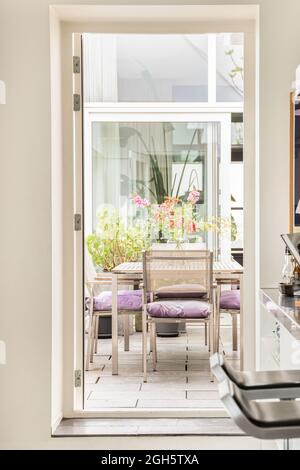 Par la porte, vue sur les chaises élégantes et la table avec des fleurs dans un vase situé dans la salle à manger sur la terrasse de la maison moderne Banque D'Images