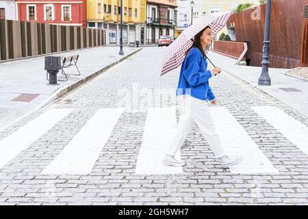 Femme afro-américaine tranquille faisant du yoga aérien avec des soies et équilibre avec bras étirés sous le pont en ville Banque D'Images