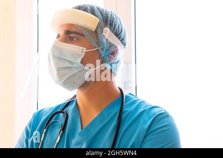 Médecin avec écran facial en plastique de protection pendant que vous travaillez en clinique et que vous regardez loin Banque D'Images