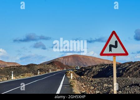 Panneau d'avertissement de route à double virage situé près de l'autoroute asphaltée contre les collines et ciel bleu nuageux à Fuerteventura, Espagne Banque D'Images