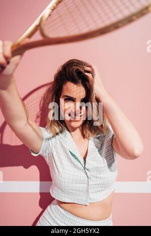 Jeune Sportswoman avec des vêtements de sport debout avec une raquette de tennis tout en regardant l'appareil photo Banque D'Images