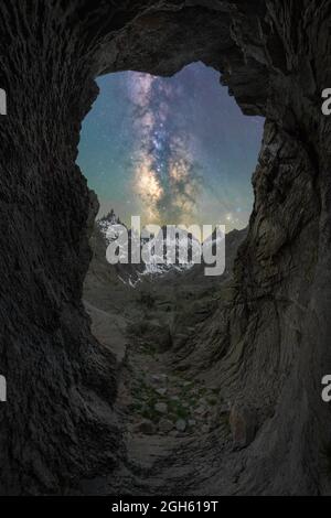 À travers la caverne, vue sur les montagnes enneigées et le ciel étoilé avec galaxie et gaz interstellaire au coucher du soleil Banque D'Images