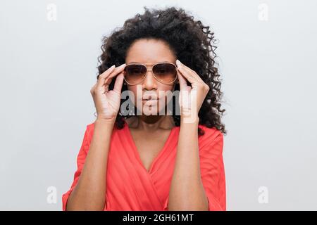 Jeune femme afro-américaine tendance avec cheveux bouclés en rouge et lunettes de soleil regardant l'appareil photo Banque D'Images