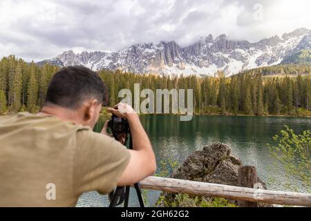 Vue arrière d'un photographe masculin en voyage méconnaissable prenant des photos d'un lac calme dans les Dolomites Mountains Banque D'Images