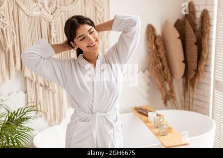 Une femme heureuse porte un peignoir blanc qui s'étire les mains dans une salle de bains moderne Banque D'Images