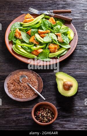 salade de saumon à l'avocat aux épinards et au poivre vert sur une assiette rustique brune avec fourchette et couteau sur une table en chêne tourbière, régime méditerranéen sain, vie verticale Banque D'Images