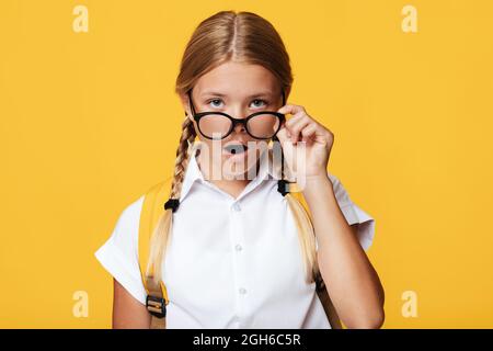 Surprise adolescente blanche mignon fille blonde avec des queues de porc et sac à dos, ouvre la bouche prend des lunettes Banque D'Images