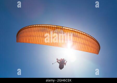 Parapente orange en tandem contre un ciel bleu, jour ensoleillé. Banque D'Images