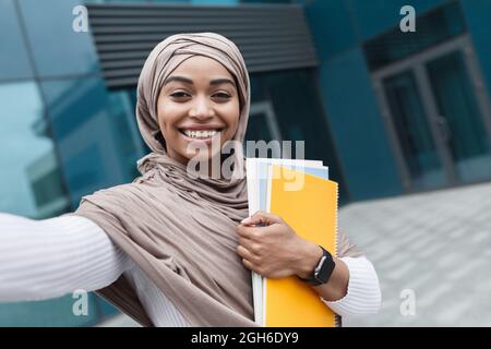 Heureux heureux joli musulman africain étudiant américain dans hijab avec des livres regarde la webcam et prend la photo Banque D'Images