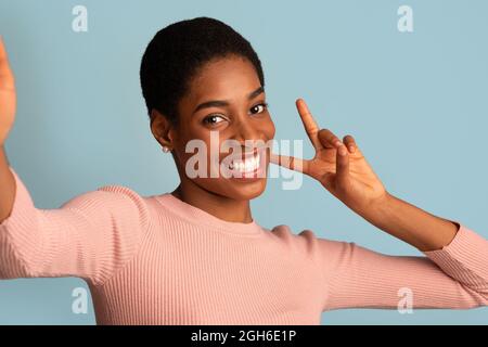 Joyeuse jeune Black femme prenant Selfie et faisant des gestes de paix à Camera Banque D'Images