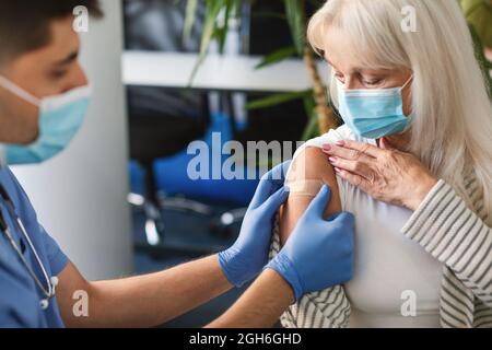 Senior Lady se faire vacciner contre Covid, docteur appliquant le plâtre Banque D'Images